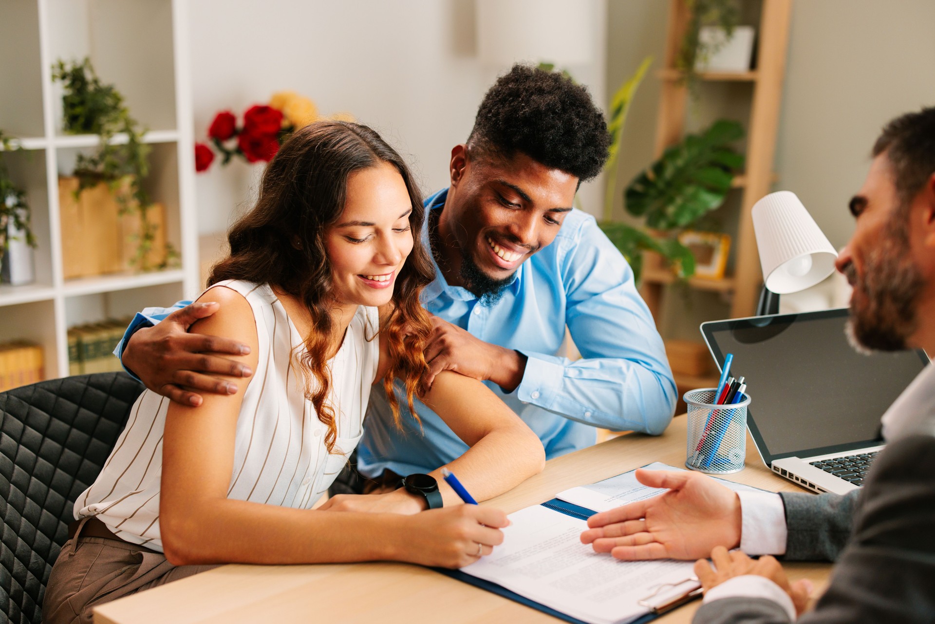 Young Latin American couple signing a contract with an agent in the office